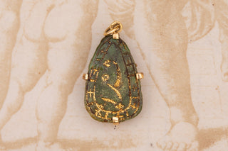 Green stone pendant with gold accents on a beige background
