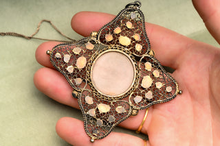 Baroque devotional pendant held in the hand for scale