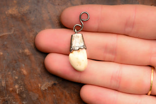 Deer tooth pendant held in the hand for scale